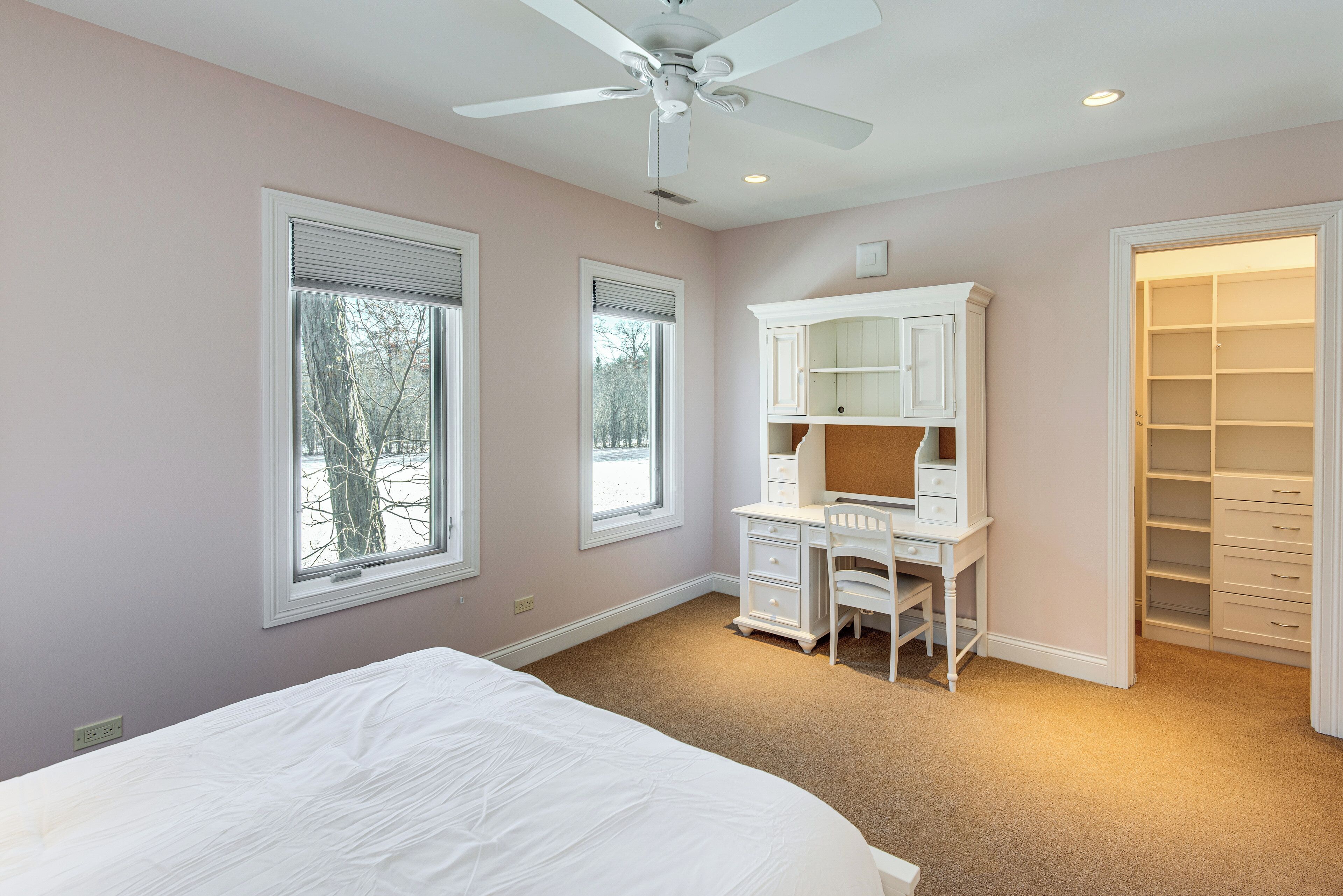 A bedroom with a bed, a desk, a chair, a wardrobe, and a ceiling fan.