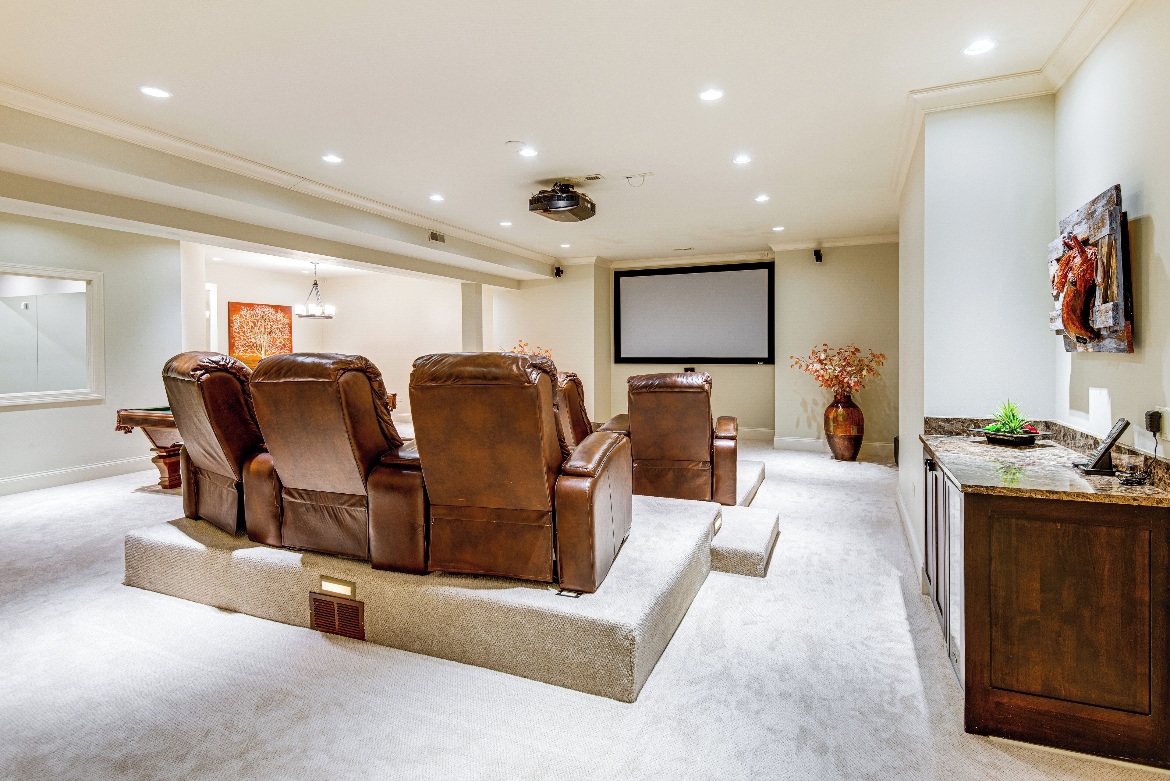 Une salle de cinéma privée équipée de fauteuils en cuir inclinables, d’un grand écran et d’un meuble en bois.