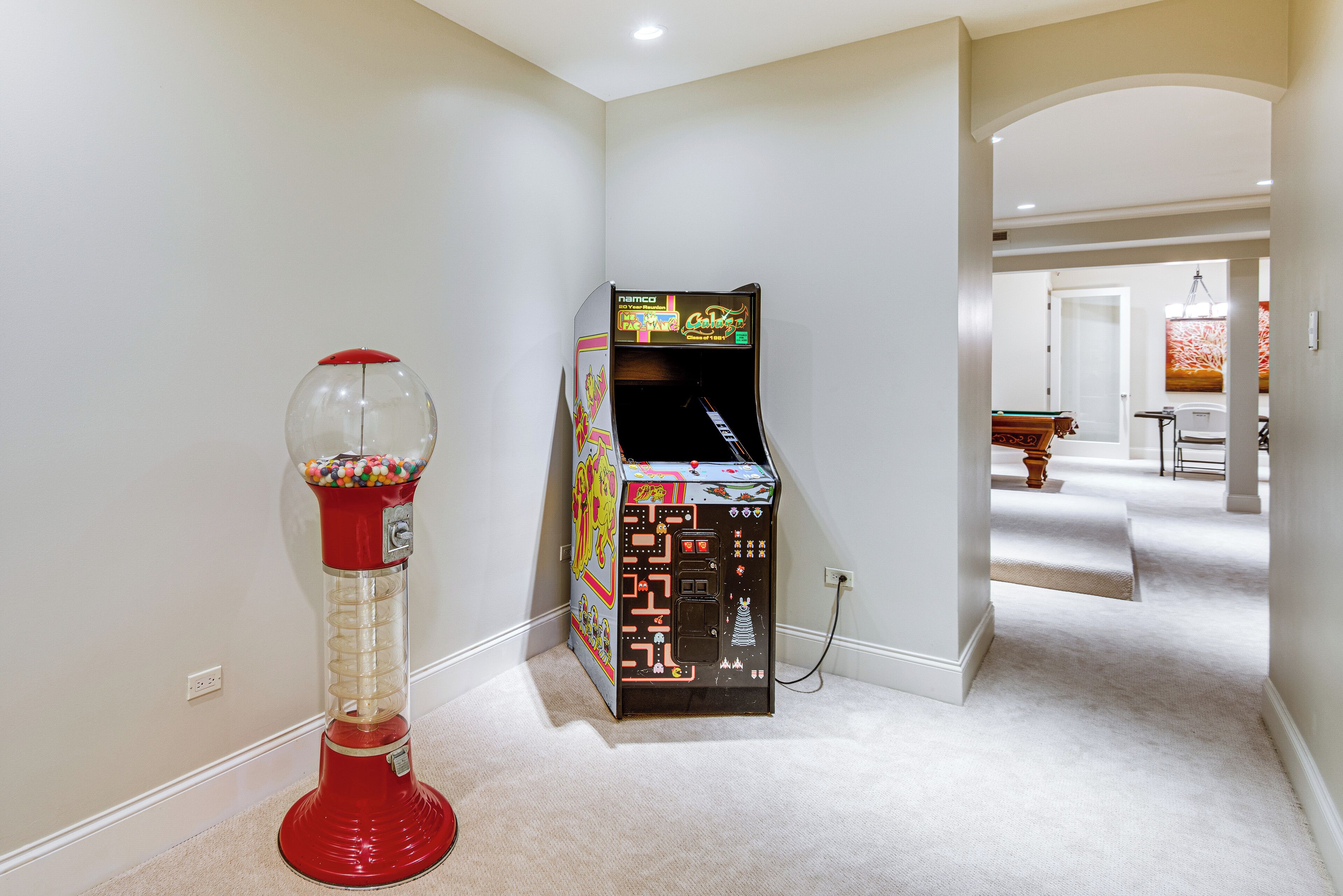 A hallway with a red gumball machine and a vintage arcade game.