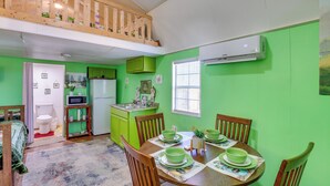 A dining area with a wooden table set for four, a kitchen with green cabinets, and a loft bedroom with a wooden railing. - Cozy Cabin in Overton Glamping Community w/ Perks! (Overton)