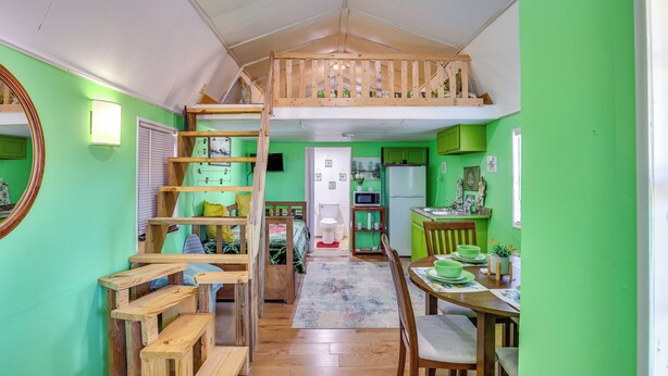 A room with a loft bed, a dining area with a table and chairs, and a kitchen area with a refrigerator and microwave. - Cozy Cabin in Overton Glamping Community w/ Perks! (Overton)