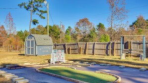 A small, single-story building with a sloped roof, a fenced yard, and a green lawn area. - Cozy Cabin in Overton Glamping Community w/ Perks! (Overton)