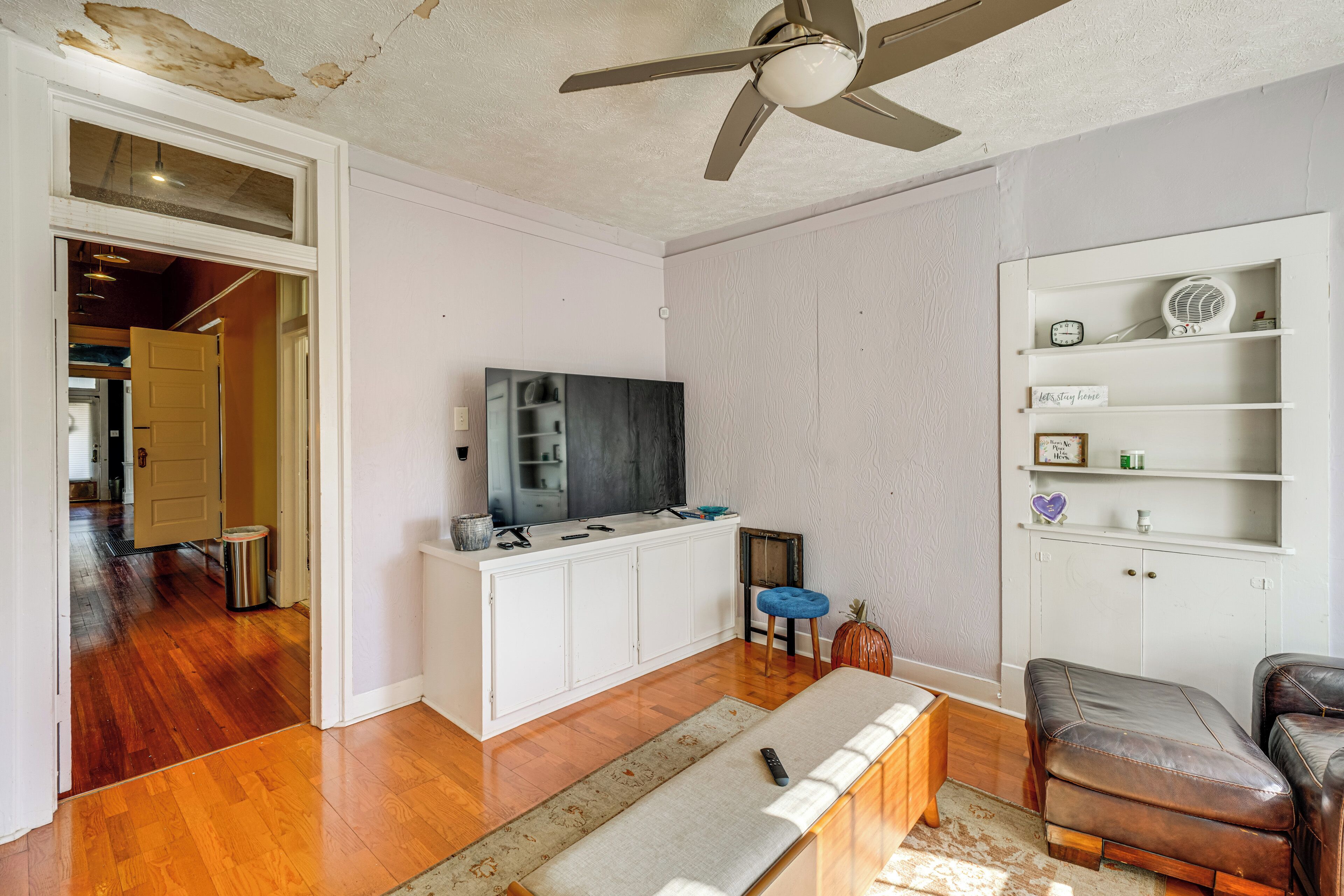 A living room with a TV, white cabinets, a ceiling fan, and a wooden floor.