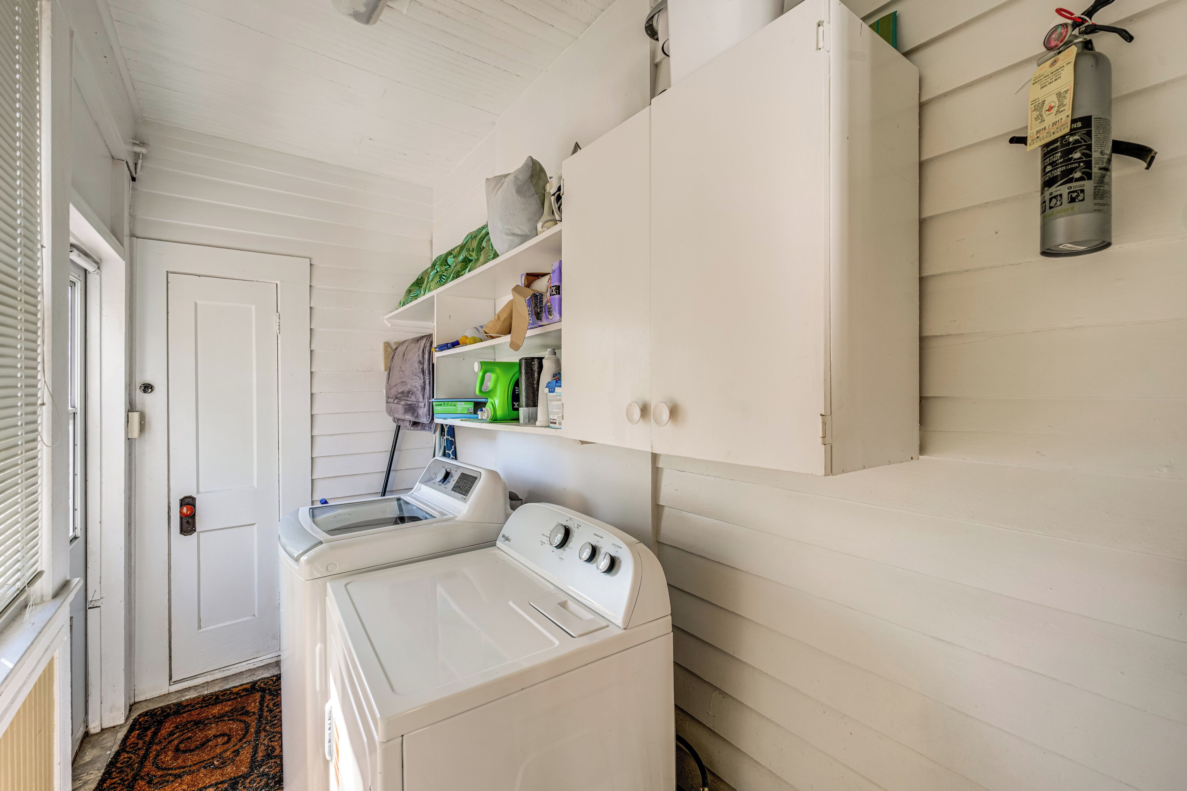 A laundry room with a front-loading washer and dryer, a white door, and a fire extinguisher mounted on the wall.