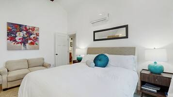 Um quarto bem arrumado com uma cama grande, um sofá, uma mesa de cabeceira com abajur e um espelho fixado na parede.