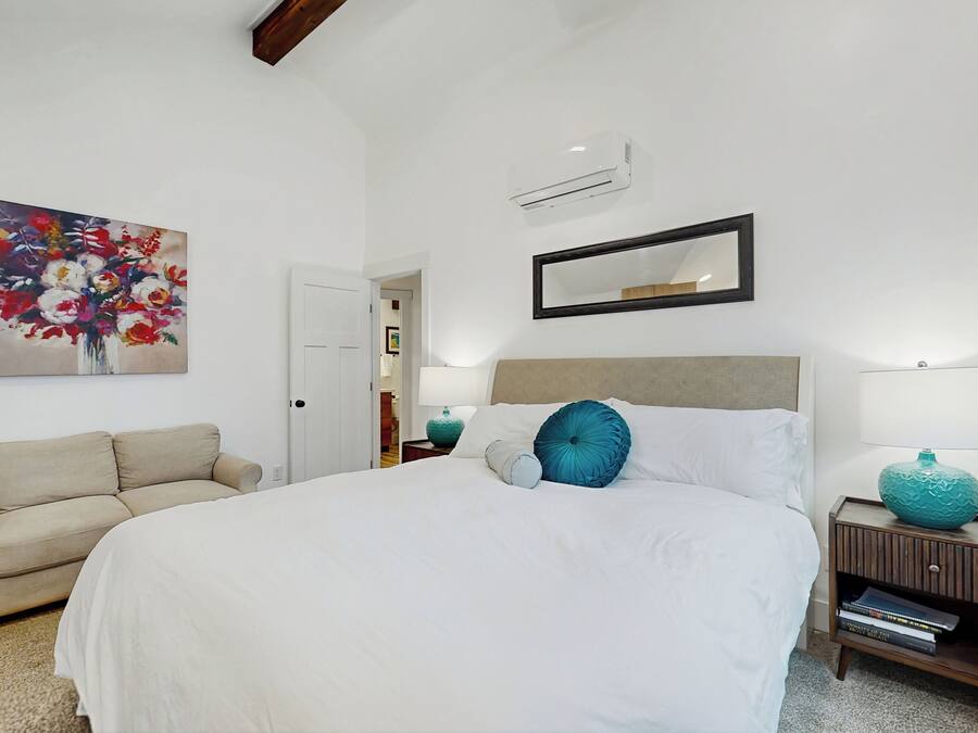Um quarto bem arrumado com uma cama grande, um sofá, uma mesa de cabeceira com abajur e um espelho fixado na parede.