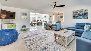 Een ruime woonkamer met een blauwe bank, een bijzettafeltje en een blauwe loungestoel. Aan de muur hangt een schilderij en er is een plafondventilator.