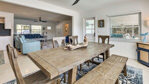 Een ruime woonkamer met een houten eettafel, een blauwe bank en een plafondventilator.