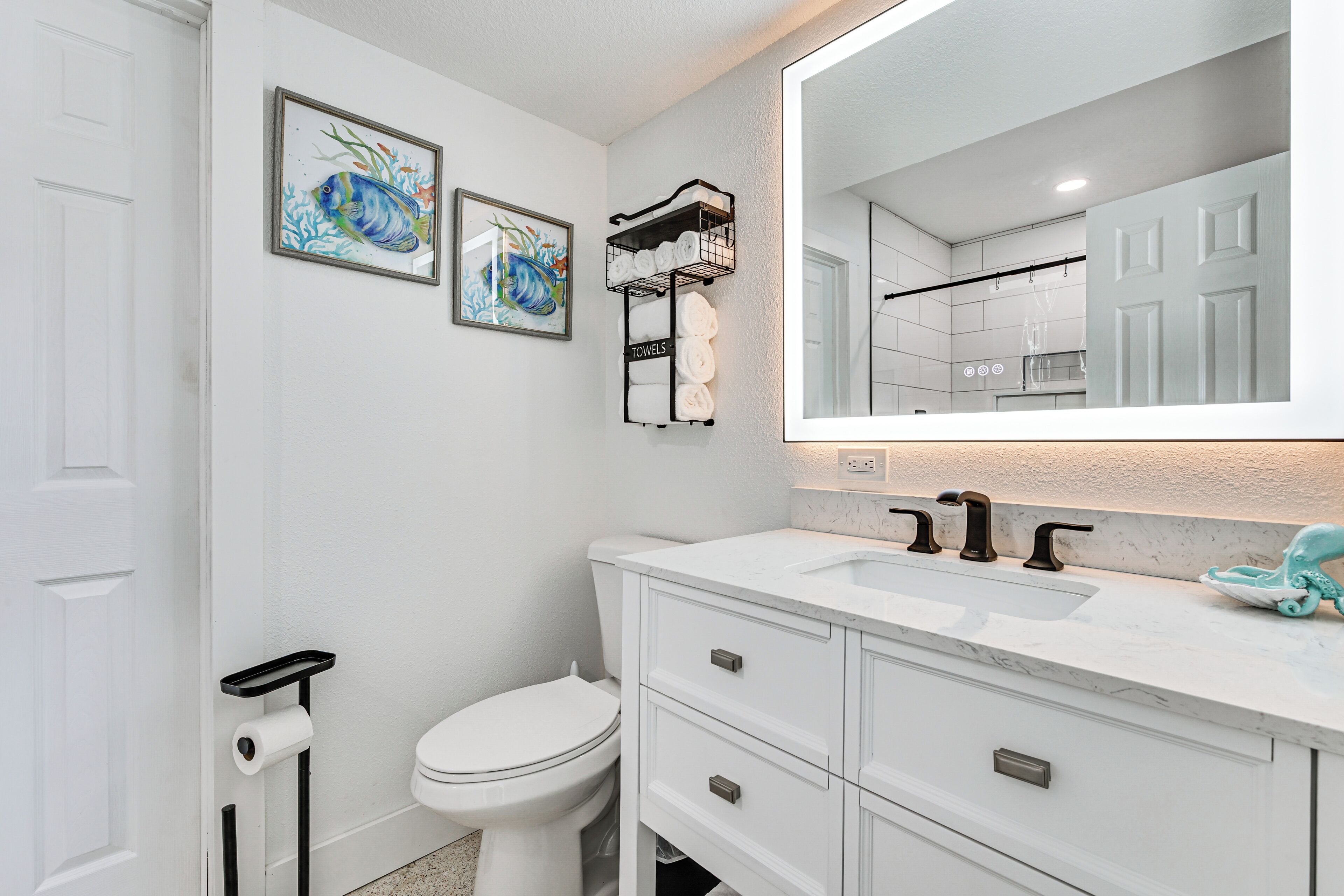 A bathroom with a white toilet, a sink with a mirror above it, and two framed pictures on the wall.