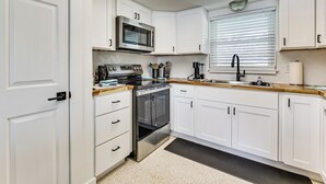 Een moderne keuken met witte kasten, roestvrijstalen apparatuur en een raam met zonwering.