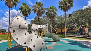 A playground with climbing structures and a slide, surrounded by palm trees and a fenced area. - Pool, Spa & Patio! Spacious Villa Near WDW (Davenport)