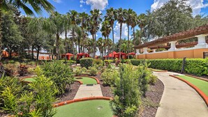 A golf course with a pathway, palm trees, and a building with red awnings. - Pool, Spa & Patio! Spacious Villa Near WDW (Davenport)