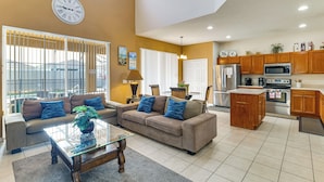 A spacious living room with a sofa, coffee table, and a kitchen area with wooden cabinets and appliances. - Pool, Spa & Patio! Spacious Villa Near WDW (Davenport)