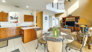 A spacious kitchen with wooden cabinets, a dining area with a glass table, and a living room with a sofa and TV. - Pool, Spa & Patio! Spacious Villa Near WDW (Davenport)
