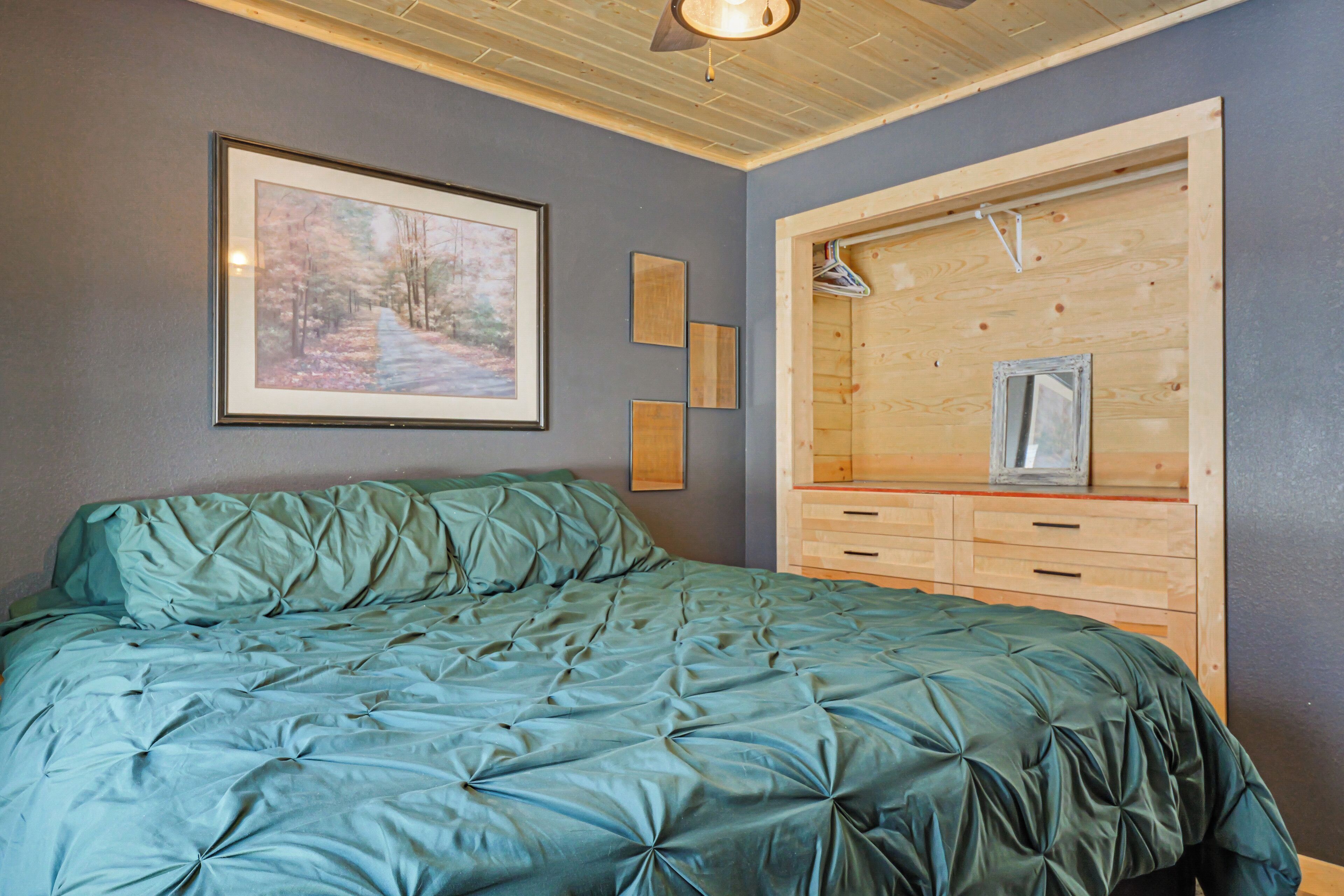 A bedroom with a bed, a wooden dresser, a framed picture on the wall, and a ceiling light.