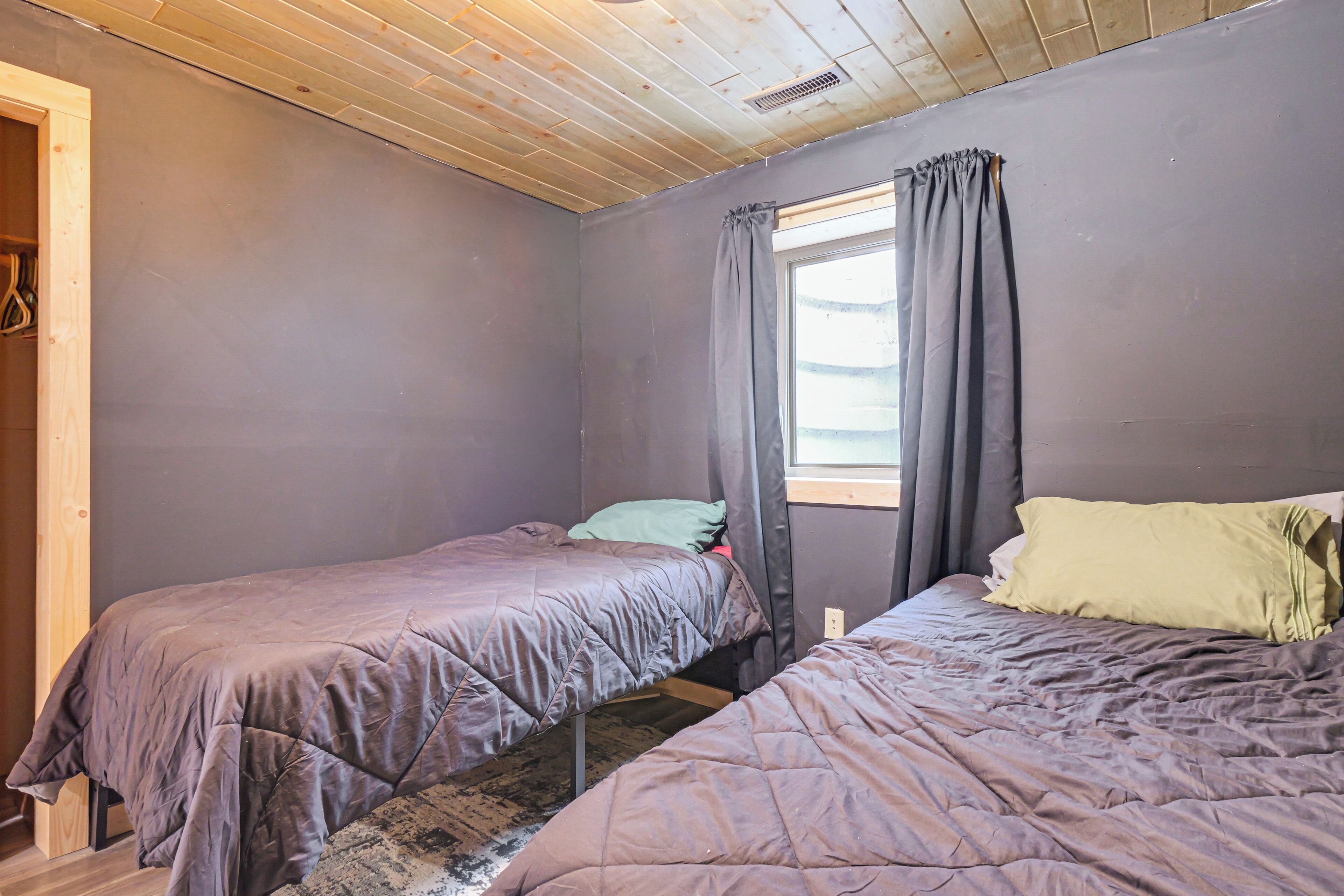 Een kamer met twee bedden, een raam met gordijnen en een houten plafond.