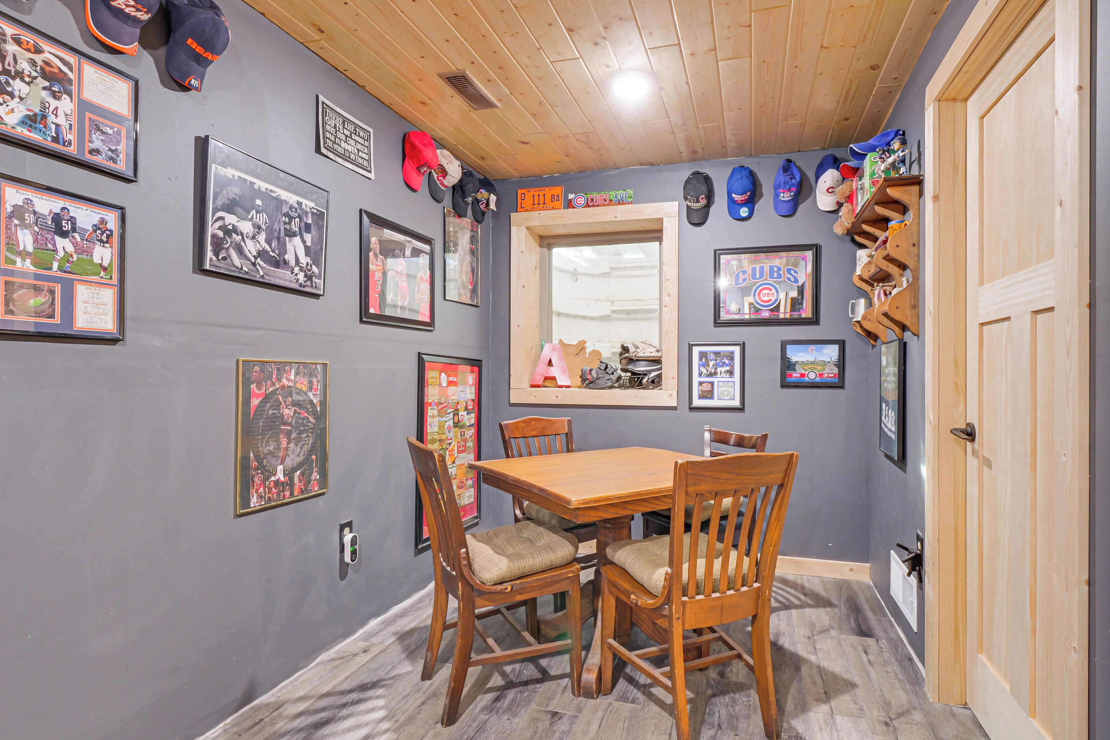 A room with a wooden dining table and chairs, framed sports memorabilia on the walls, and a mirror with a 'CUBS' sign.