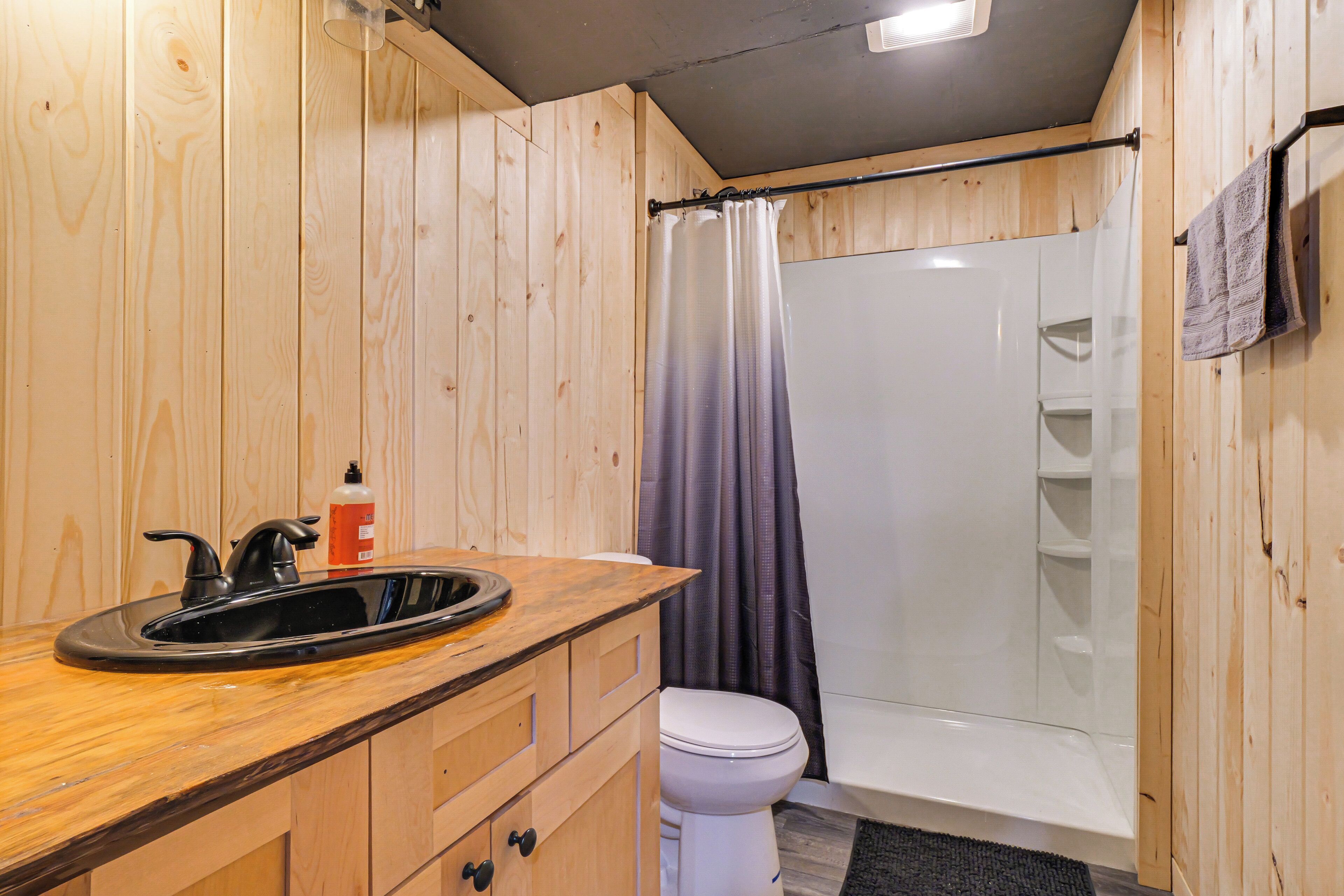 A bathroom with wooden walls, a black sink, a white toilet, and a shower area.
