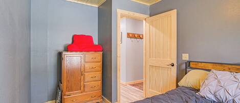 A bedroom with a wooden dresser, a bed with a quilted cover, and a door leading to another room.