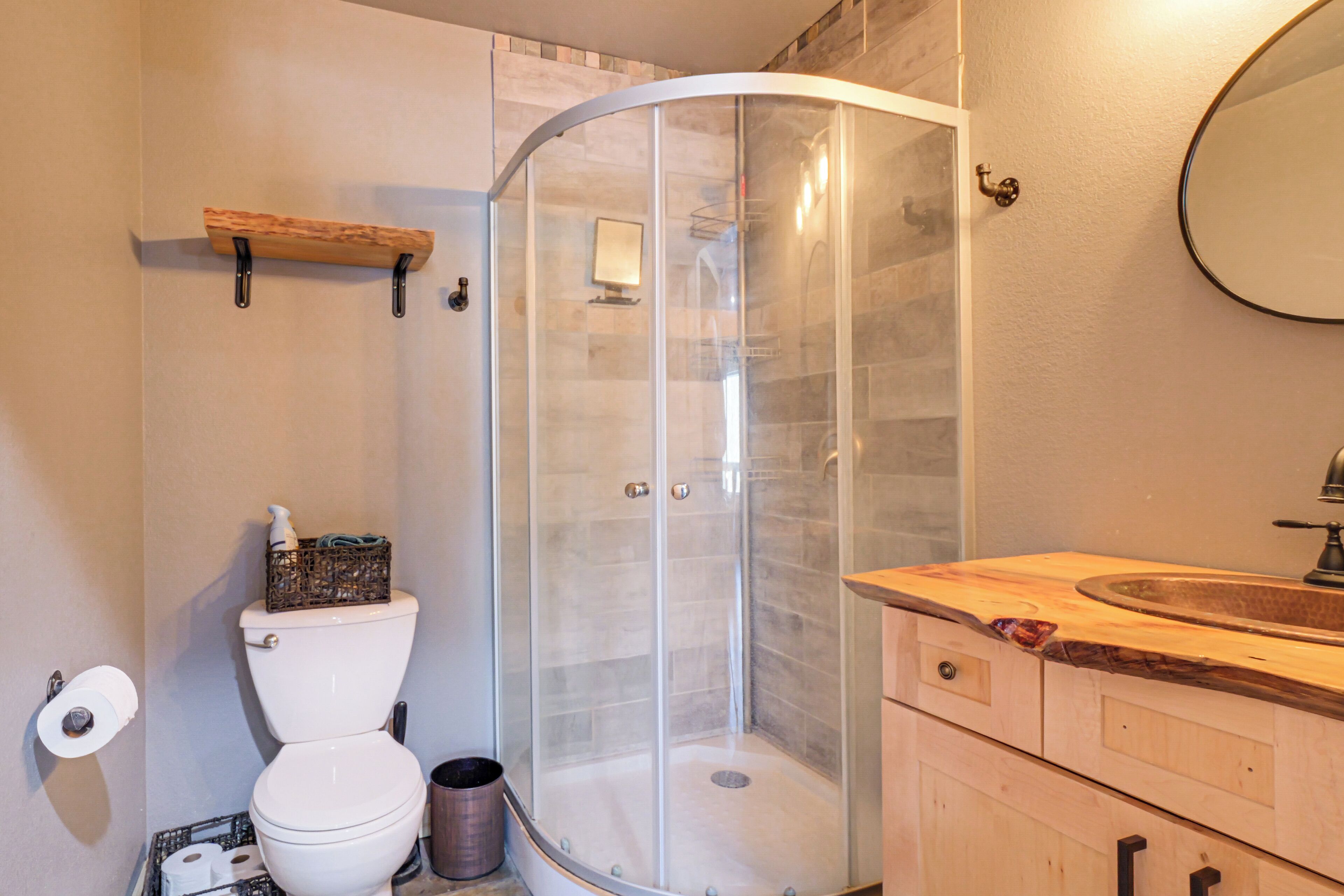 A bathroom with a toilet, a glass-enclosed shower, a wooden vanity with a sink, and a mirror.
