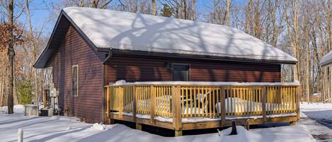 A wooden cabin with a snow-covered roof and a wooden deck.