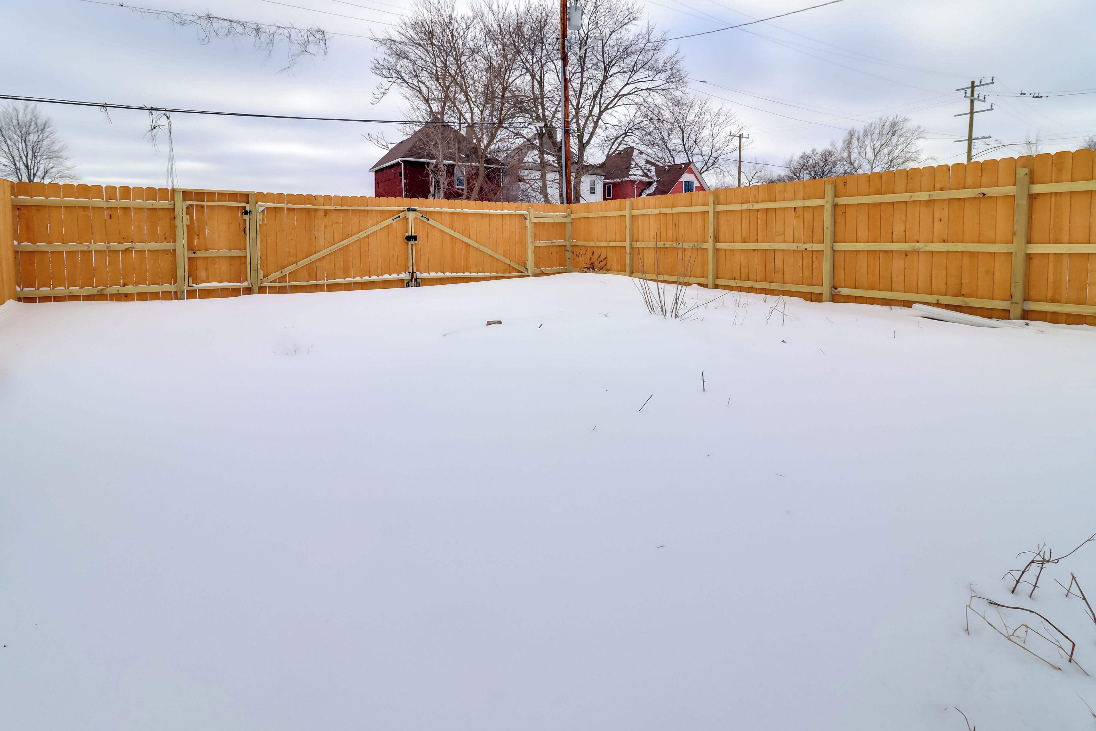 Patio nevado con cerca de madera y portón.
