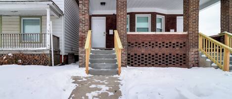 A two-story building with a brick facade, a front porch, and a staircase leading to the entrance.