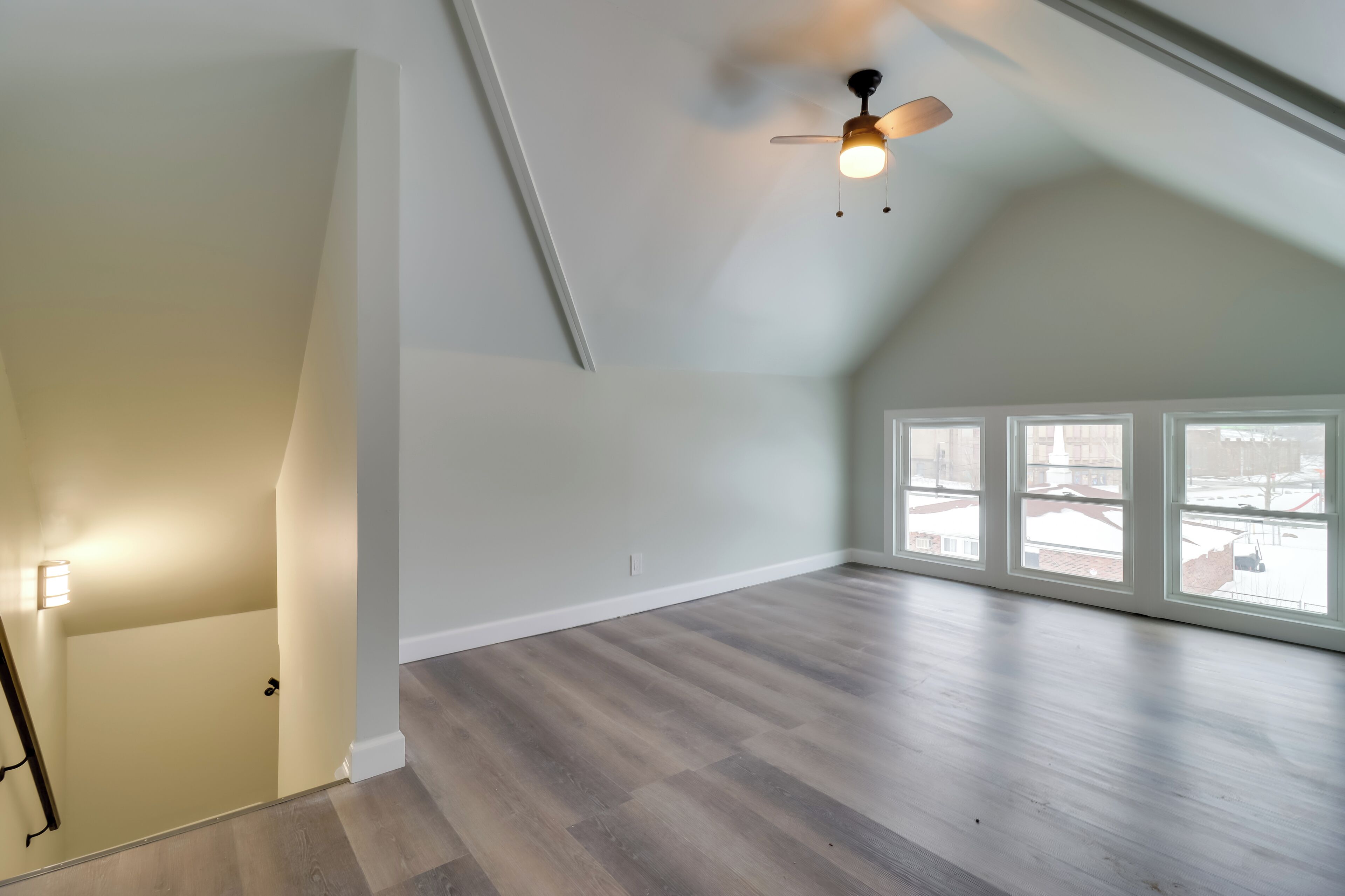 A spacious room with a sloped ceiling, large windows, and a ceiling fan.