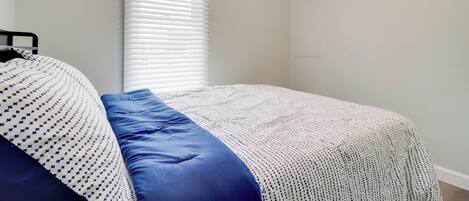 A bedroom with a bed, a window with blinds, and a plain wall.