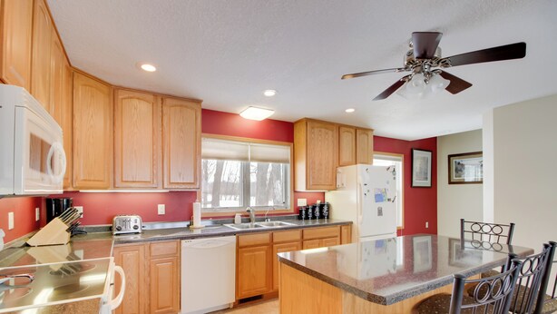 A kitchen with wooden cabinets, a granite countertop, a built-in dishwasher, a refrigerator, and a ceiling fan. - Family Nature Haven! Lakefront Pelican Lake Duplex (Ashby)