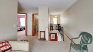 A spacious living area with a staircase, a green chair, and a small table. - Family Nature Haven! Lakefront Pelican Lake Duplex (Ashby)