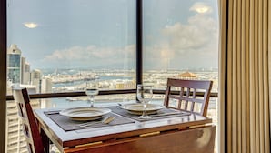 A dining table with plates, cutlery, and glasses set for two, overlooking a cityscape through a large window. - Harbor View + Pool Access: Downtown Honolulu Gem! (Honolulu)