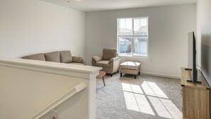 A spacious living room with a large window, a flat-screen TV on a wooden stand, and a beige sofa. - Pet-friendly Yard! Family Home in Bakersfield (Bakersfield)
