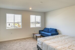 Een slaapkamer met een bed, een blauwe bank, twee ramen en een klein tafeltje.
