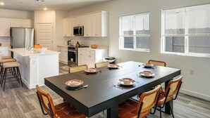 A modern kitchen with white cabinets, a central island, and a dining area with a dark table and wooden chairs. - Pet-friendly Yard! Family Home in Bakersfield (Bakersfield)