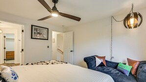 A bedroom with a large bed, a ceiling fan, a wall-mounted light fixture, and a door leading to another room. - Mcm-inspired Decor & Top Location! Tumwater Duplex (Olympia)