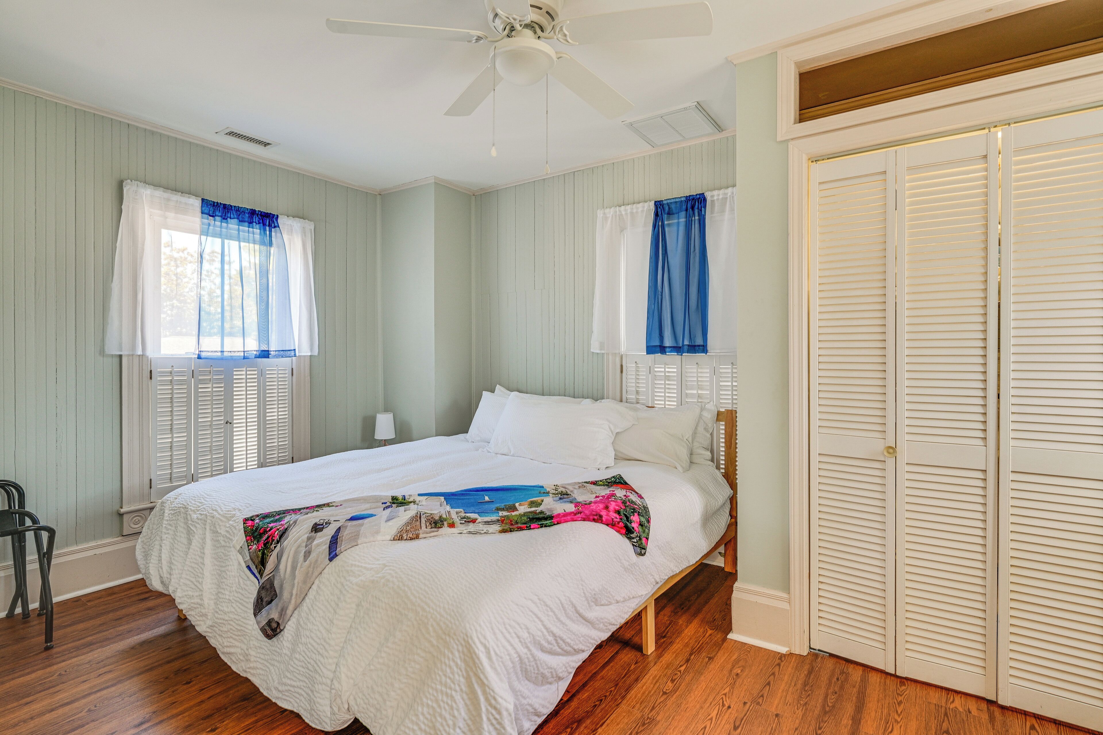 A bedroom with a bed, a ceiling fan, and a window with shutters.