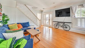 A spacious living room with a wooden floor, a blue sofa with colorful cushions, a wooden coffee table, a staircase with white railings, and a bicycle leaning against the wall. - Timeless Charm! Family Home Near Belhaven Beach (Belhaven)