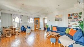 A spacious living room with a blue sofa, wooden flooring, and a bookshelf filled with books. - Timeless Charm! Family Home Near Belhaven Beach (Belhaven)