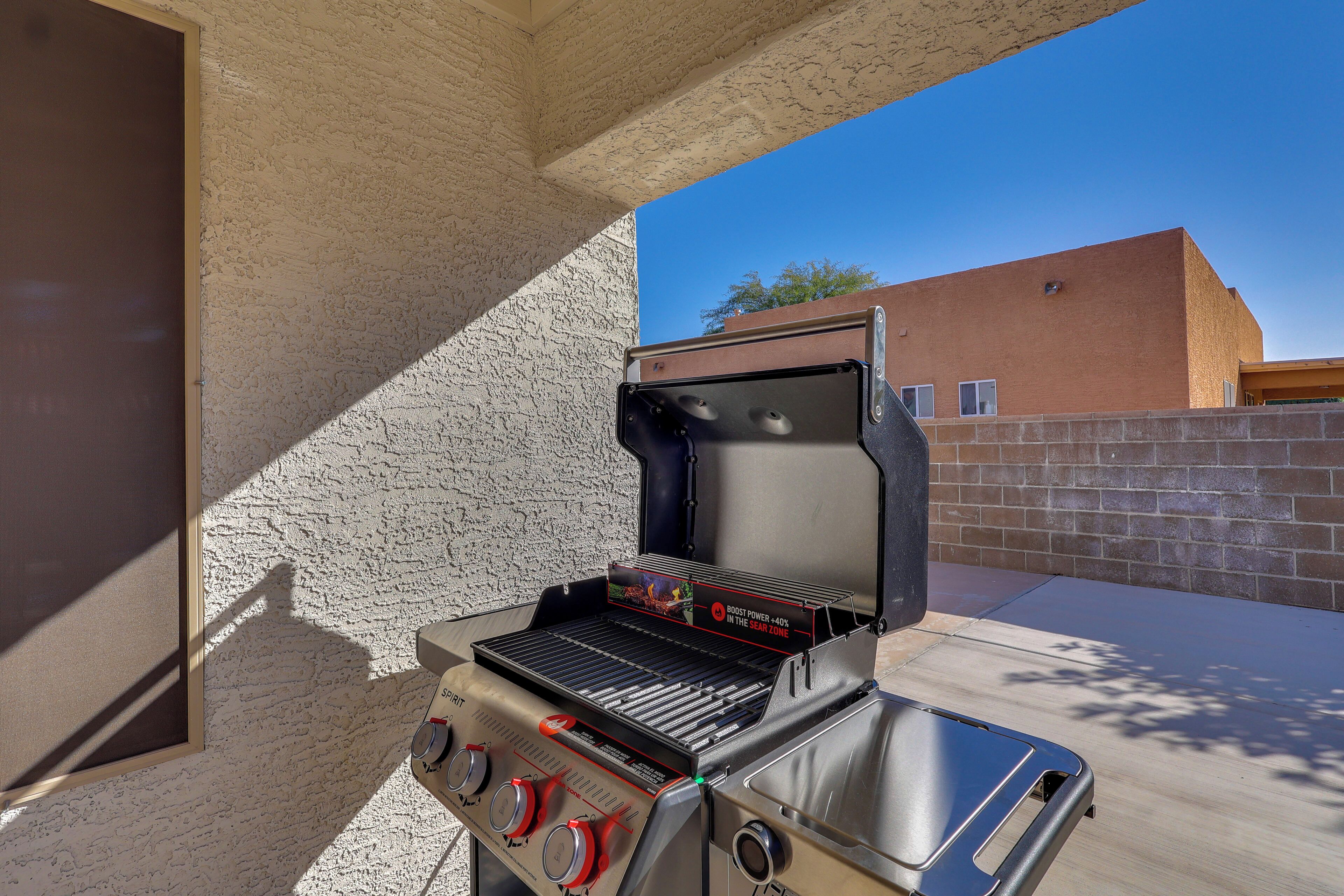 An outdoor grill with a digital display, a stainless steel sink, and a brick wall in the background.