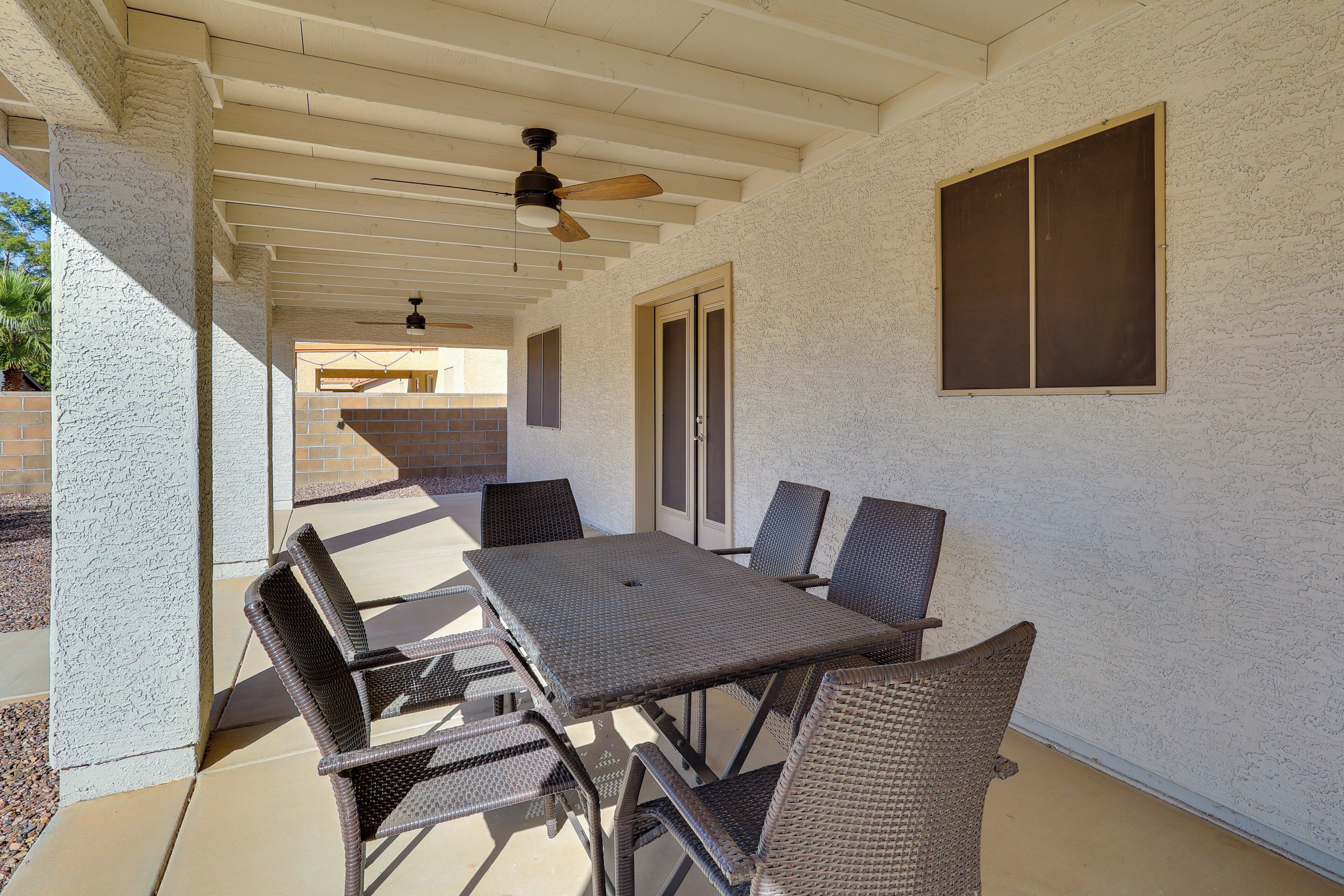 An outdoor patio with a table and chairs, a ceiling fan, and a window.