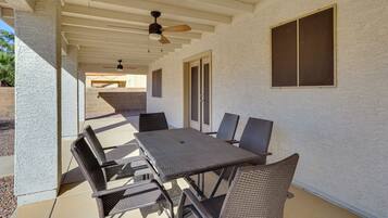 An outdoor patio with a table and chairs, a ceiling fan, and a window.