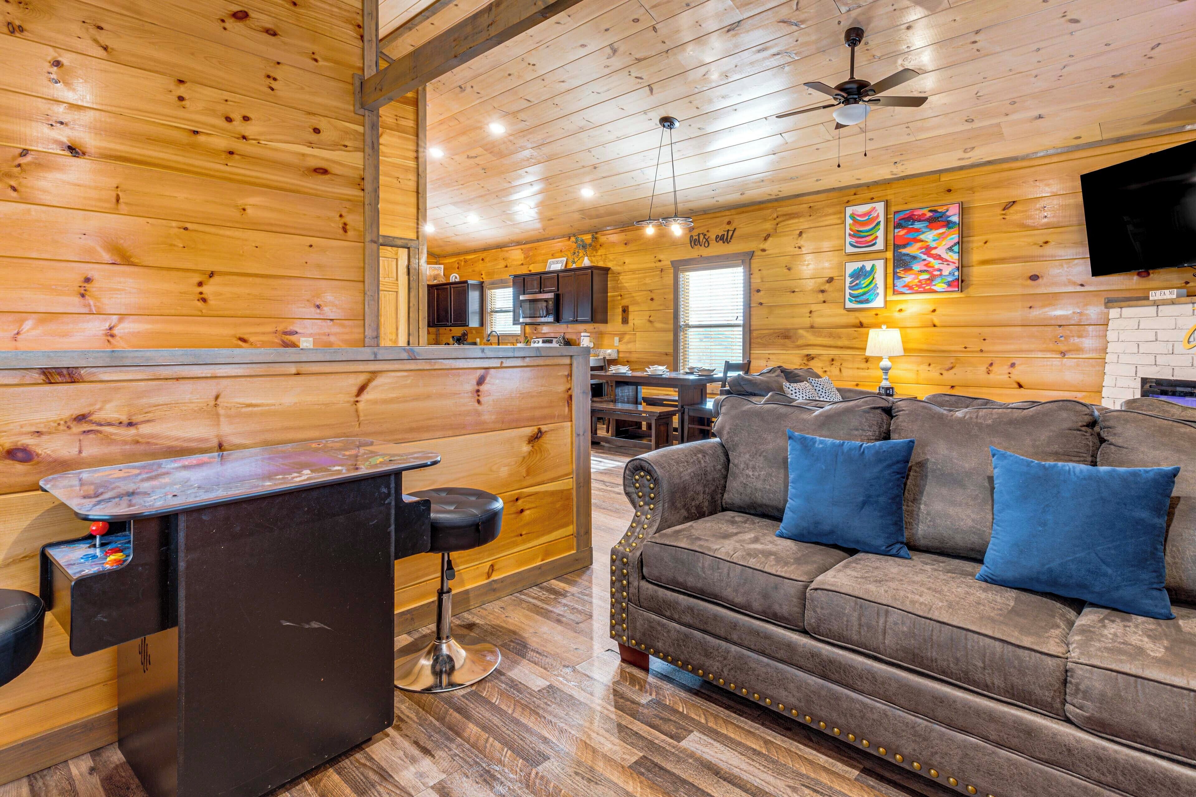 A cozy cabin interior with a wooden interior, a dining area, a sofa with blue cushions, and a bar area.