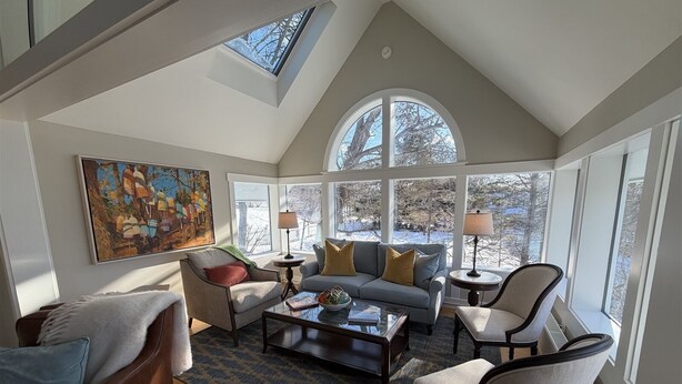 A spacious living room with a high ceiling, large windows, a cozy fireplace, and a comfortable seating area.