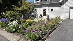 A two-story house with a front porch, a chimney, and a garden with various plants and flowers.