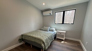 A bedroom with a bed, a nightstand, a window, and an air conditioning unit.