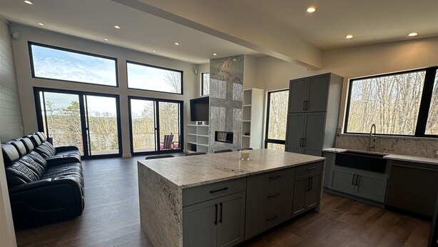 A modern kitchen with a large island, grey cabinets, and a view of trees through large windows.