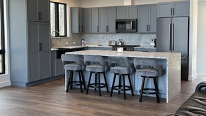 A modern kitchen with grey cabinets, a central island with bar stools, a microwave, and a refrigerator.