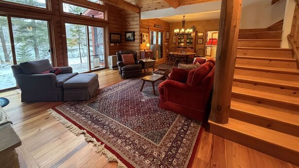 A spacious living room with a large window, wooden ceiling beams, and a red sofa.