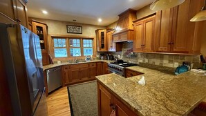 A kitchen with wooden cabinets, granite countertops, a stainless steel stove, and a window with a view of the outdoors.